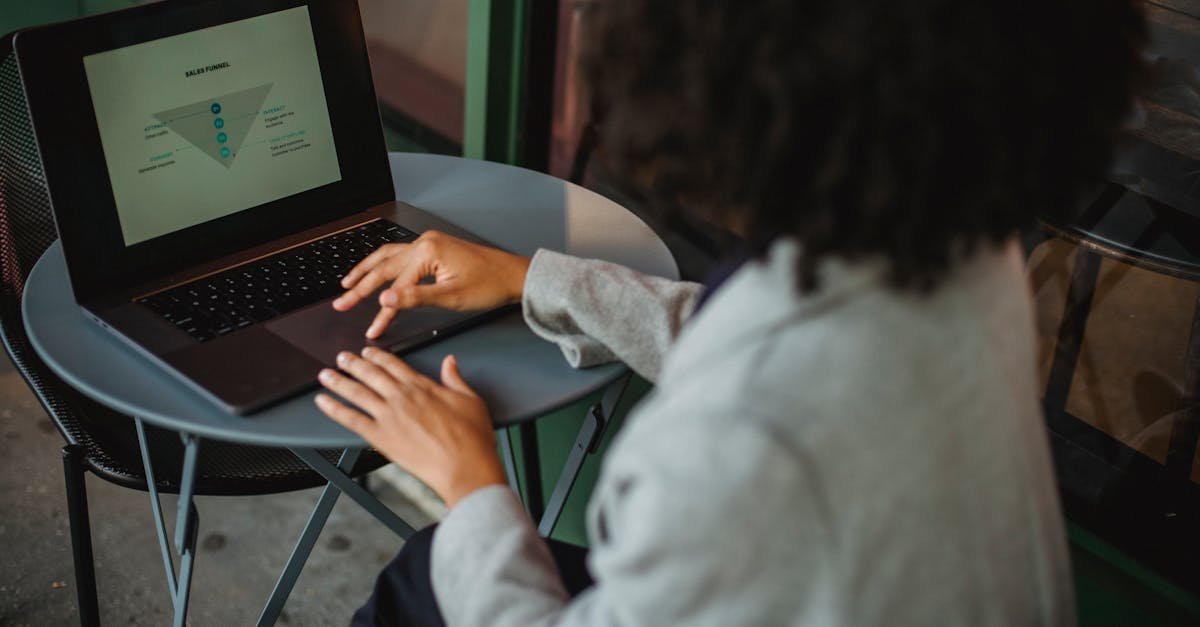 Back view of anonymous ethnic female in suit working with chart on computer while sitting at table in outdoor cafe during remote work