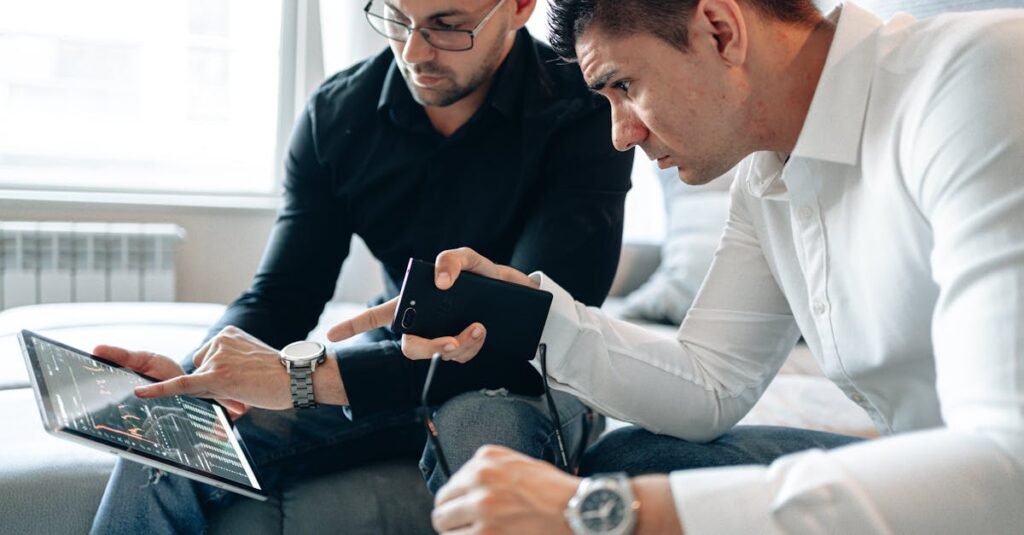 Two men analyzing financial data on a digital tablet indoors in a professional setting.