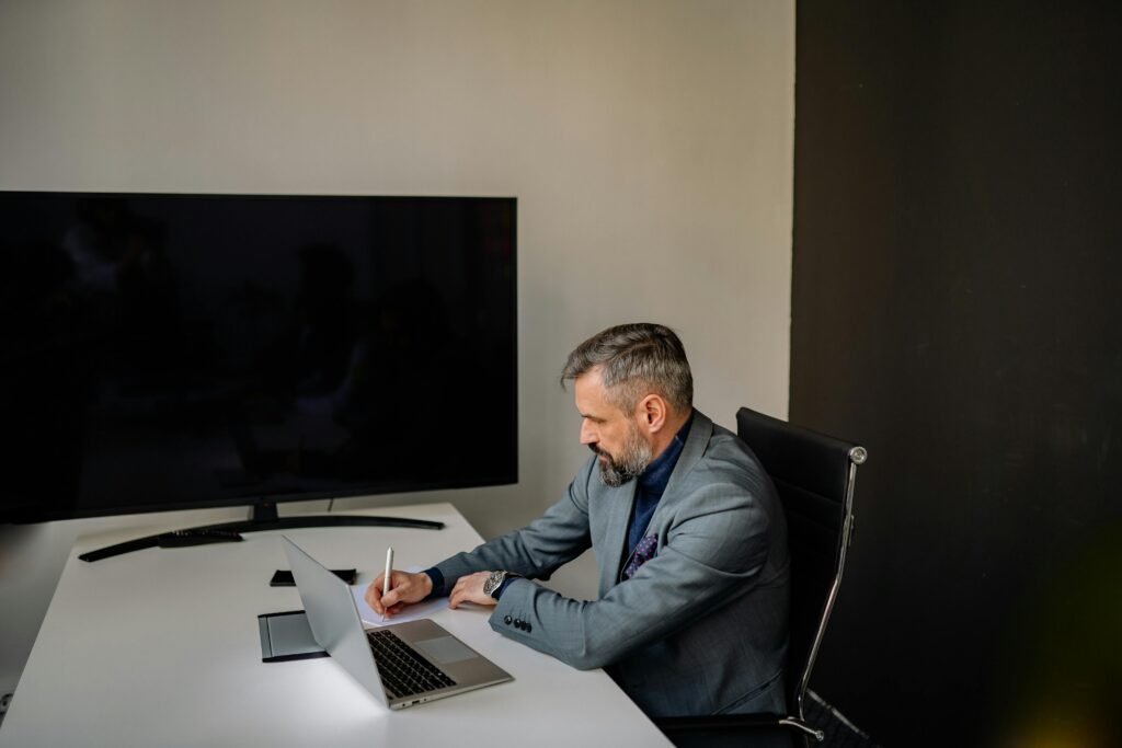 Bearded businessman in formal attire writing notes at a modern office workspace.